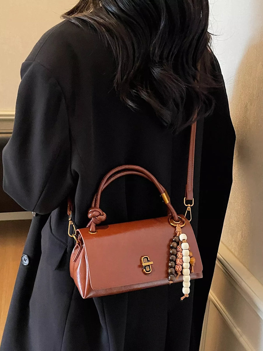 Brown leather crossbody bag with beaded charm detail and knotted handle.