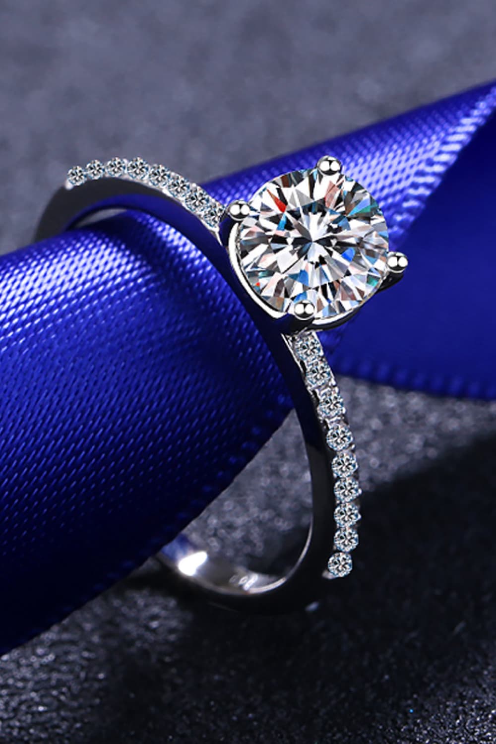 Silver moissanite ring with pavé band and solitaire center stone on blue ribbon.