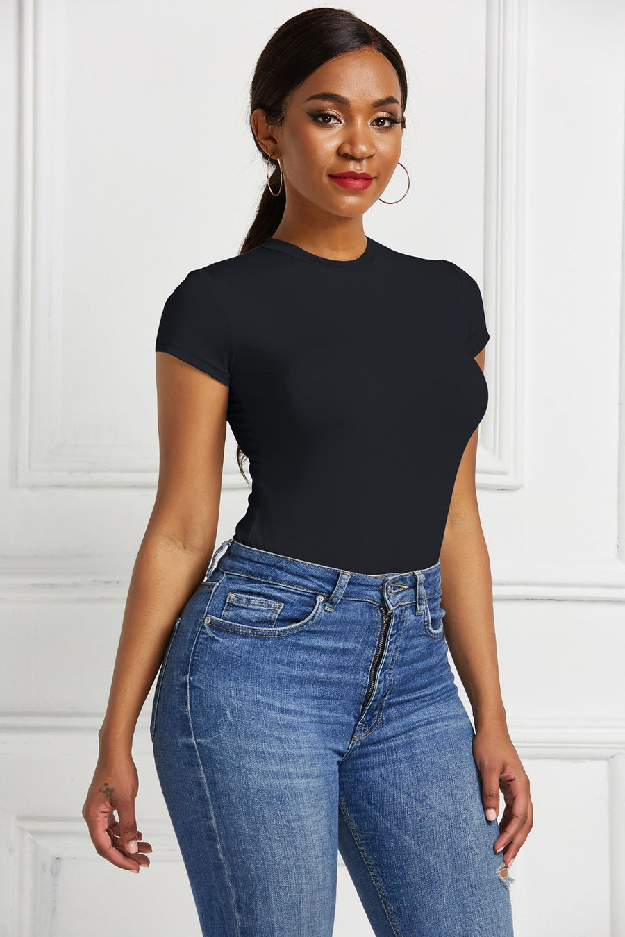 Black crew neck short sleeve bodysuit with a sculpted fit, paired with blue denim jeans.