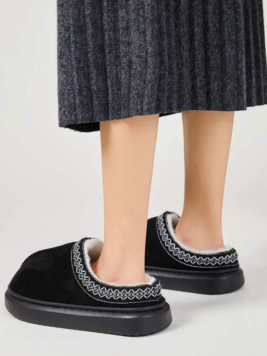 Black shearling house slippers with embroidered trim and thick soles.