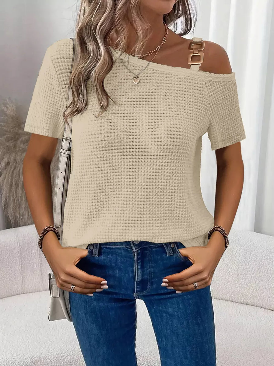 Beige waffle knit one-shoulder t-shirt with gold buckle detail and short sleeves.