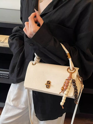 Ivory leather crossbody bag with beaded charm detail and gold clasp