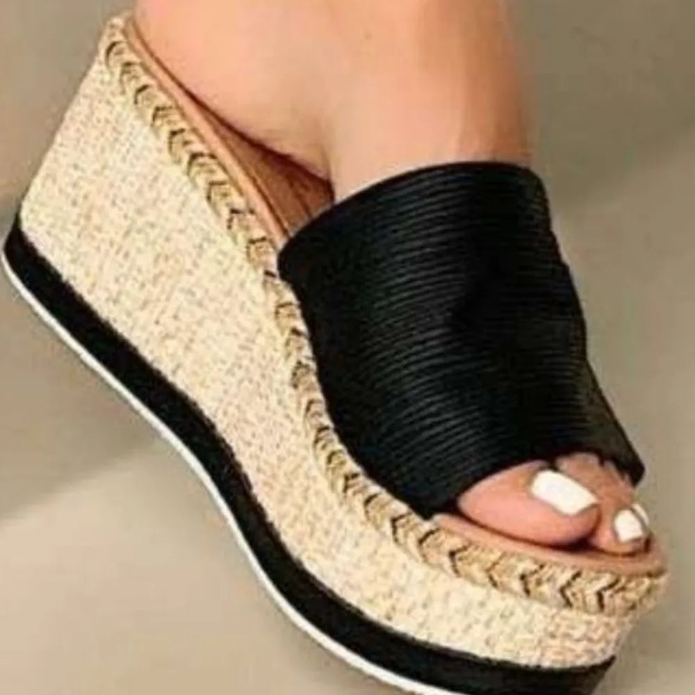 Textured platform slides in black with woven straw wedge and metallic detail.