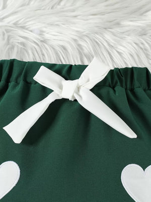Green baby skirt with white heart appliques and a white bow detail.
