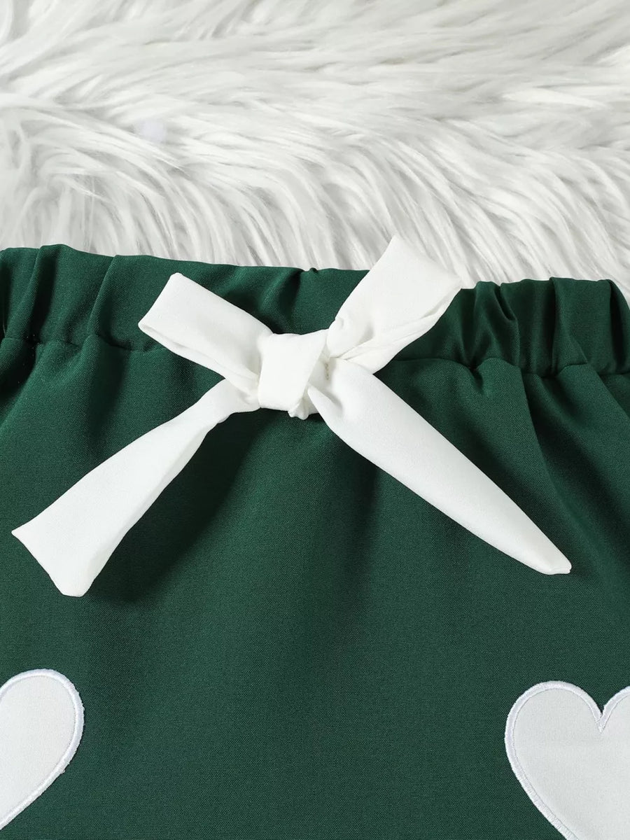 Green baby skirt with white heart appliques and a white bow detail.