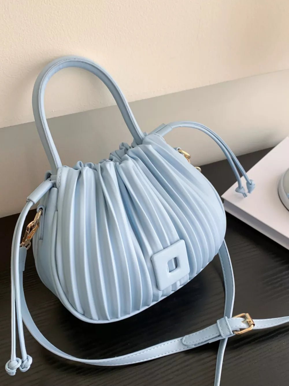 Light blue pleated bucket bag with drawstring closure and square detail
