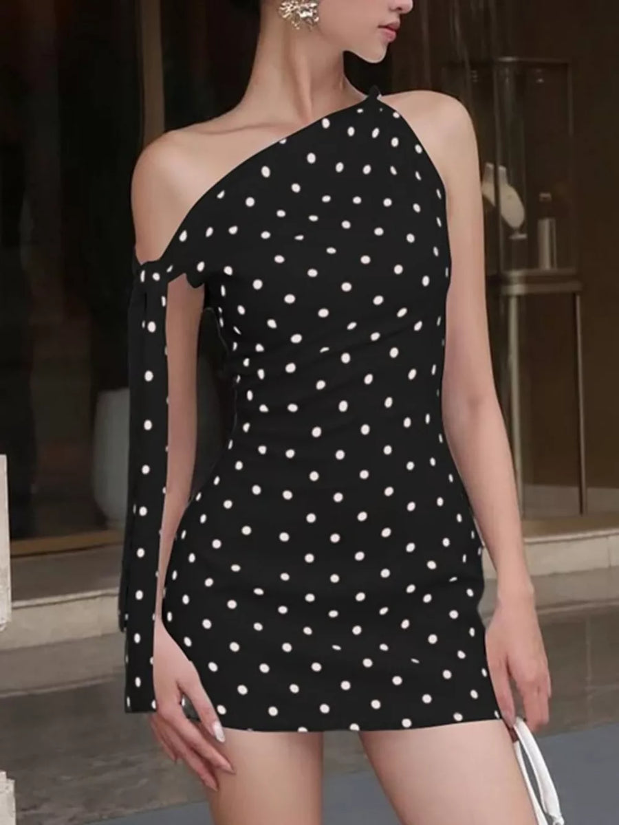 Black polka dot mini dress with asymmetrical neckline and bow detail on sleeve.