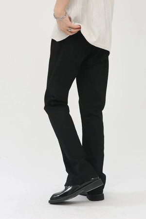 Black denim trousers with zip hem detail, styled casually.