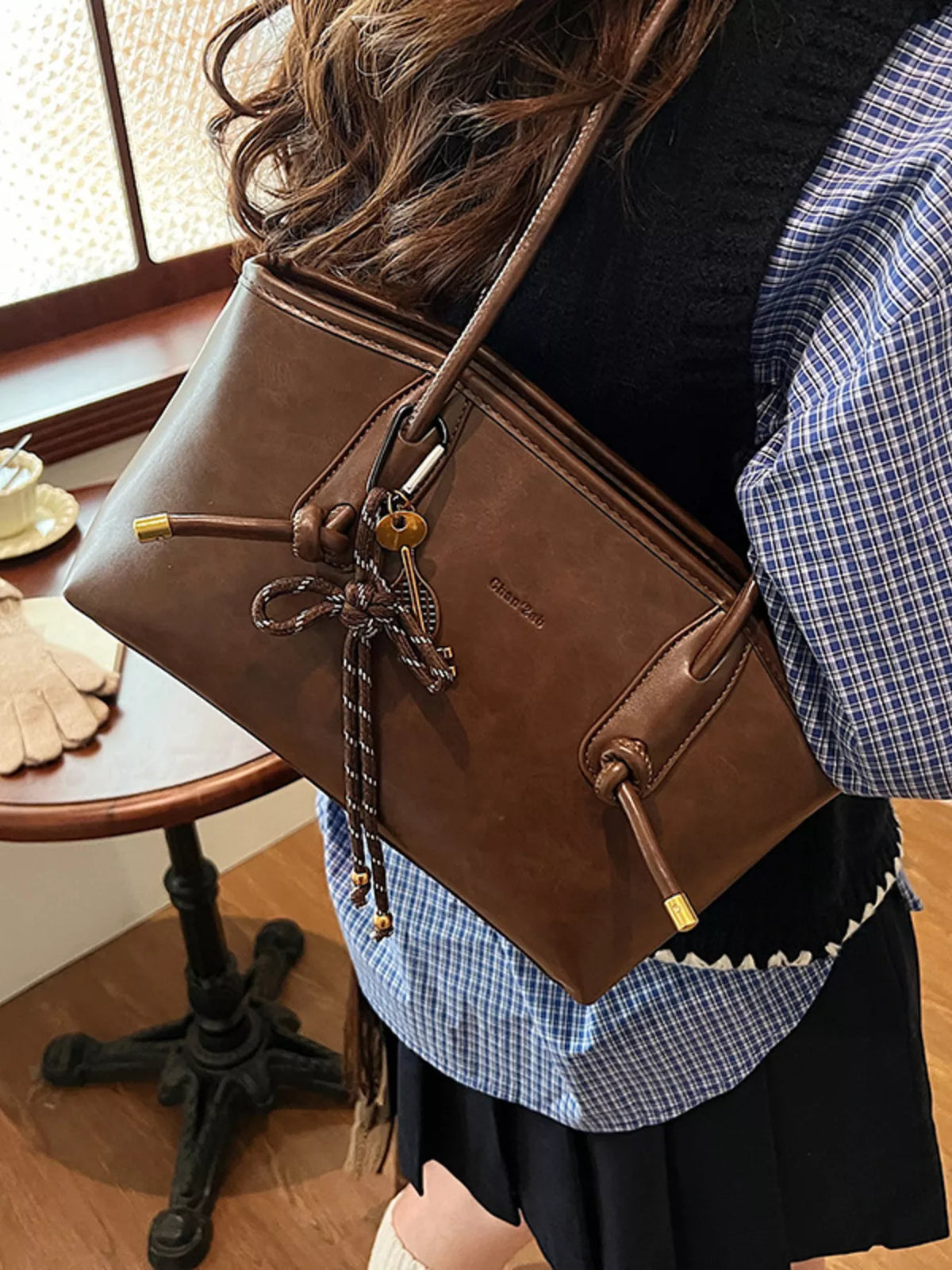 Brown leather shoulder bag with drawstring detail and gold hardware.