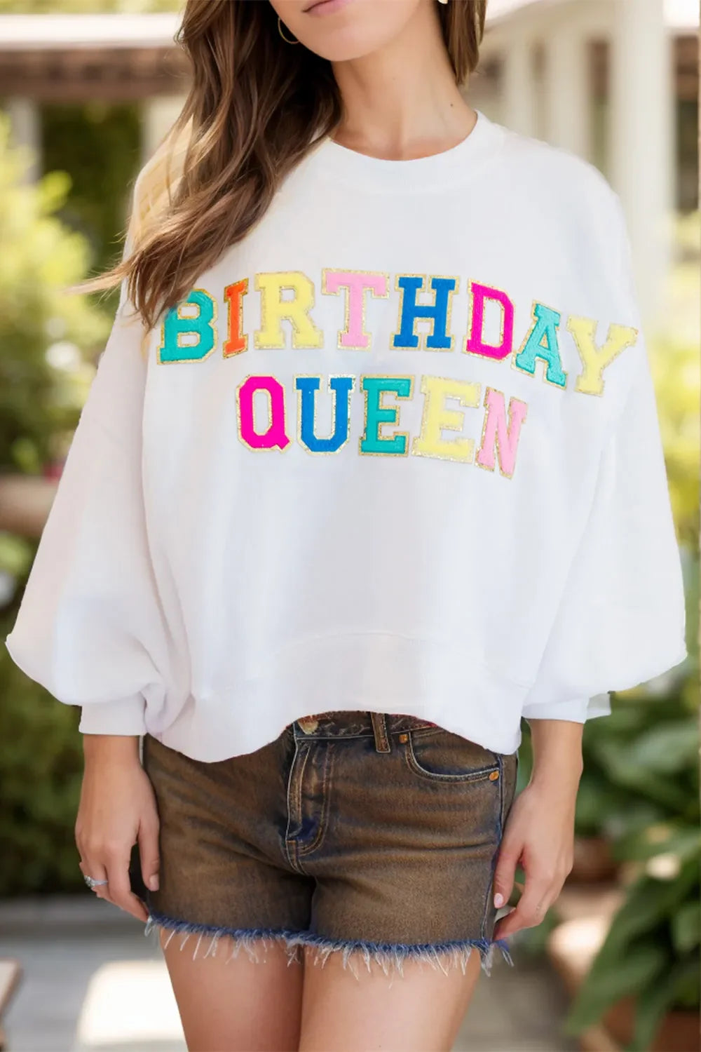 White sweatshirt with puff sleeves and colorful "Birthday Queen" applique text.