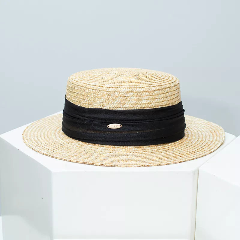 Refined straw boater hat with black ribbon detail and gold emblem.