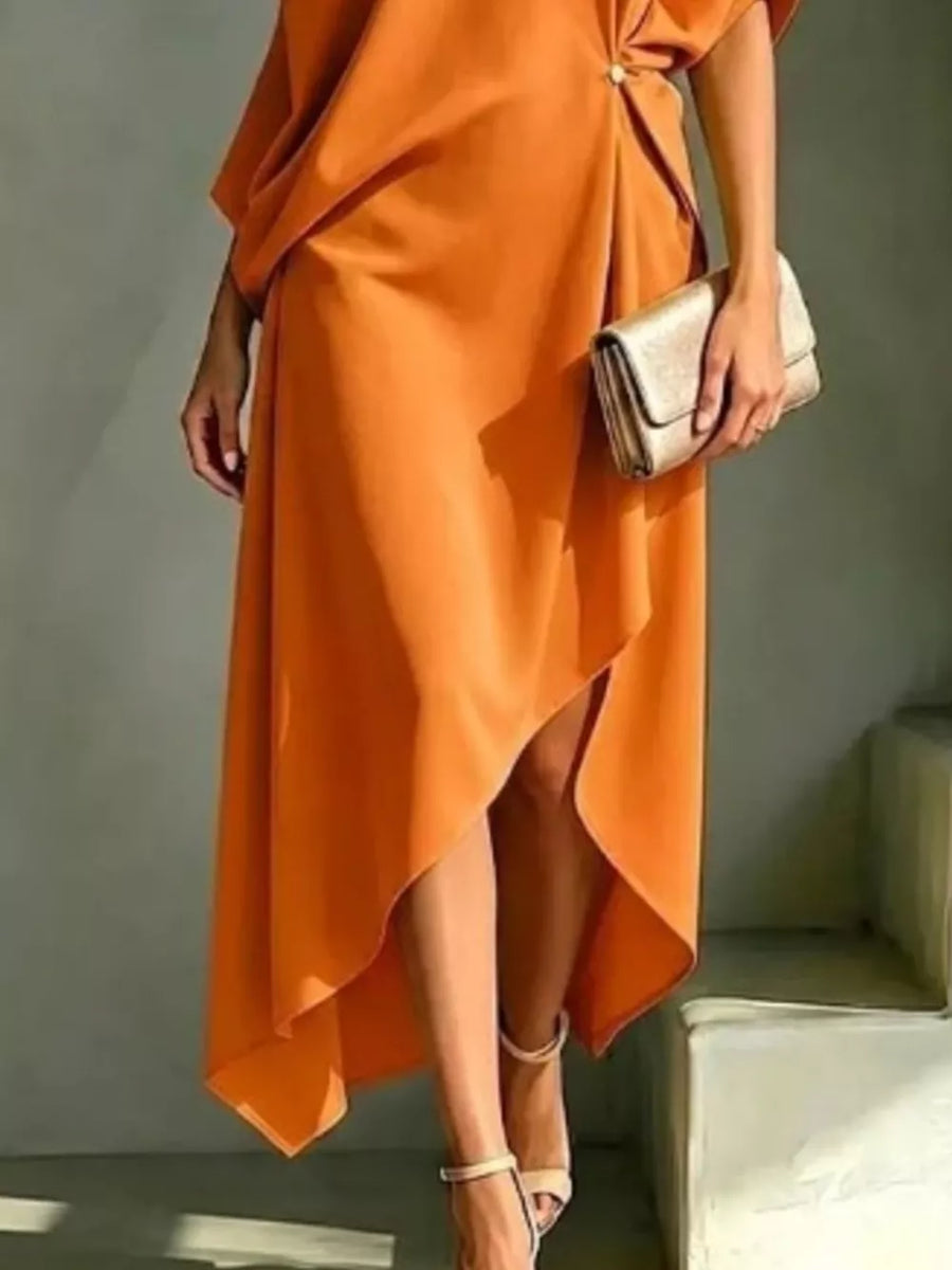 Orange asymmetrical midi dress with draped detail and gold hardware, styled with a clutch.