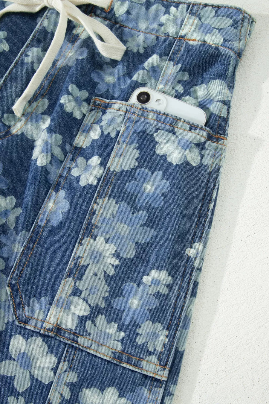 Floral drawstring barrel jeans with pockets in blue denim, featuring a daisy print and a phone in the pocket.