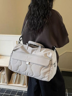 Light grey quilted duffel bag with adjustable strap and top handles.