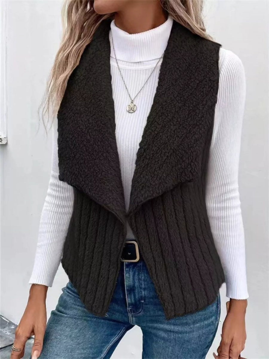 Black open front fleece vest with ribbed texture and shawl collar, styled with a turtleneck and jeans.
