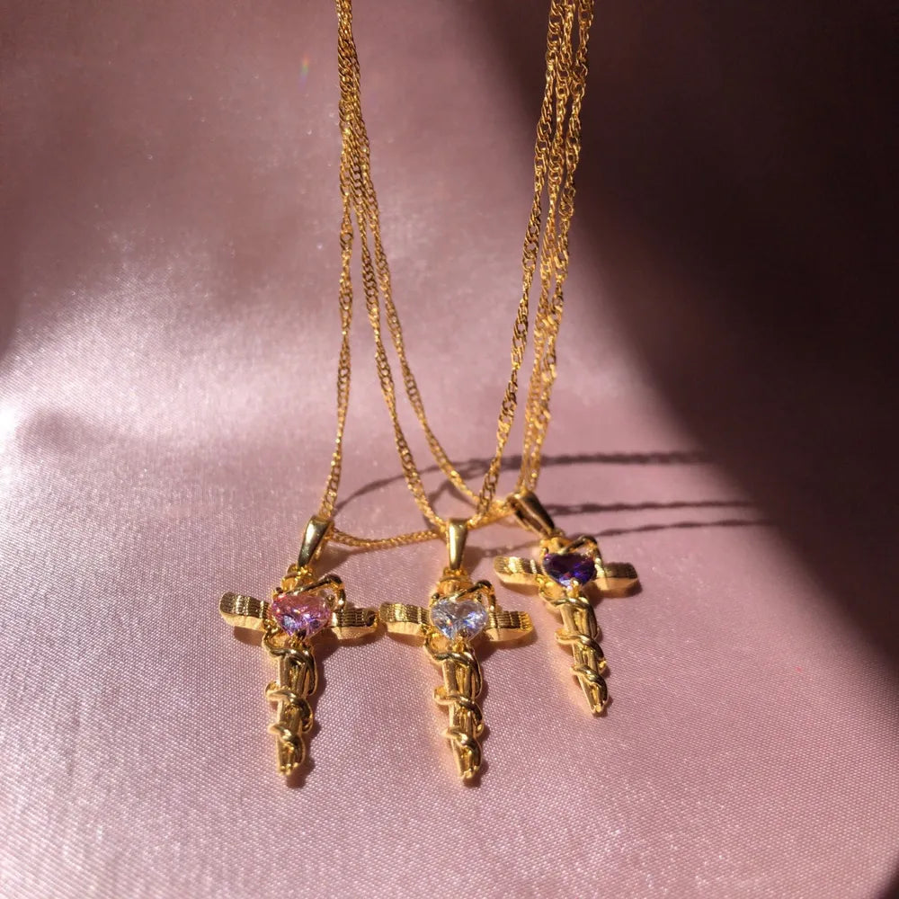 Gold-plated cross charm necklaces with heart-shaped gemstones in pink, clear, and purple.