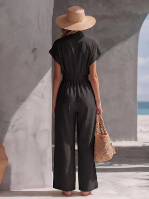 Black wide-leg jumpsuit with elastic waist and short sleeves, worn with a straw hat and bag.