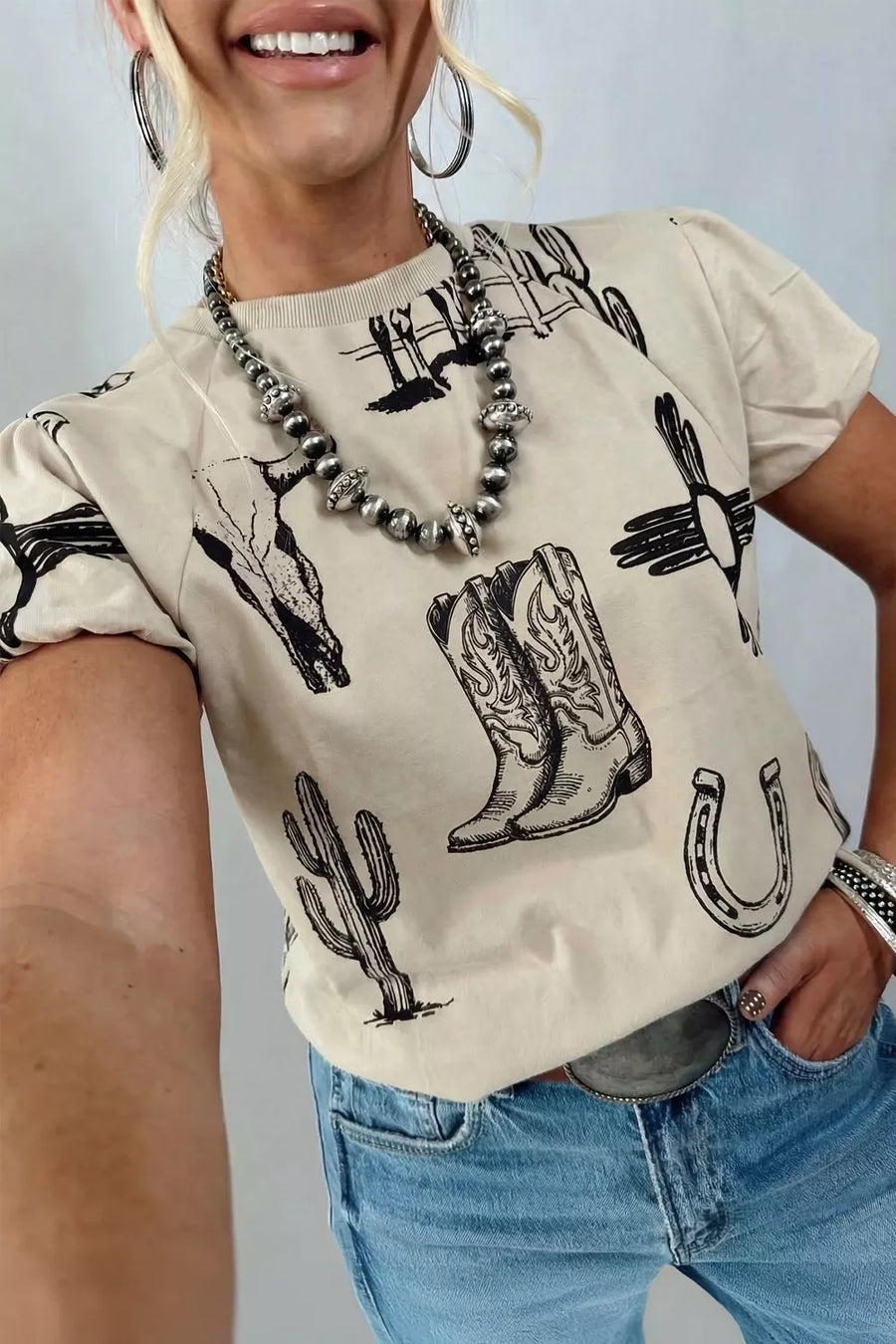Cream crew neck t-shirt with all-over western graphic print of boots, cactus, and bull skull.