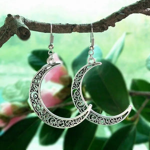 Filigree crescent drop earrings in Moon color, featuring intricate scrollwork and hanging from a branch.