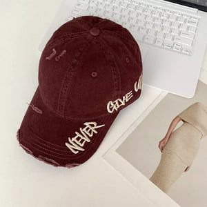 Wine Red distressed baseball cap with embroidered "Never Give Up" text and frayed details.