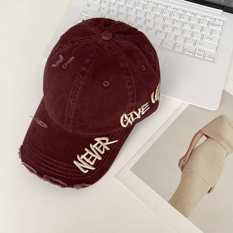 Wine Red distressed baseball cap with embroidered "Never Give Up" text and frayed details.