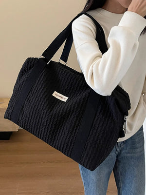 Black waffle-weave weekend bag with silver hardware and a white label.