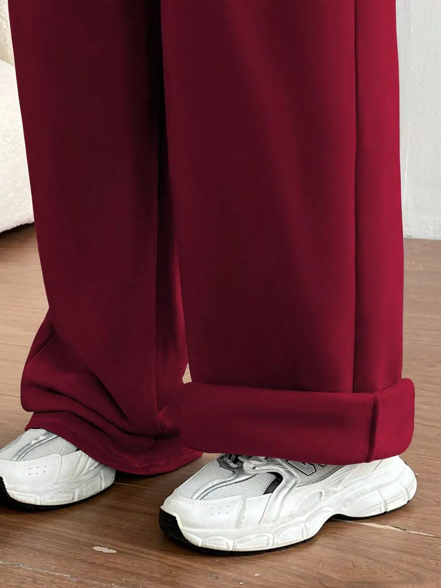 Burgundy wide-leg maternity joggers with cuffed hems, styled with white sneakers.