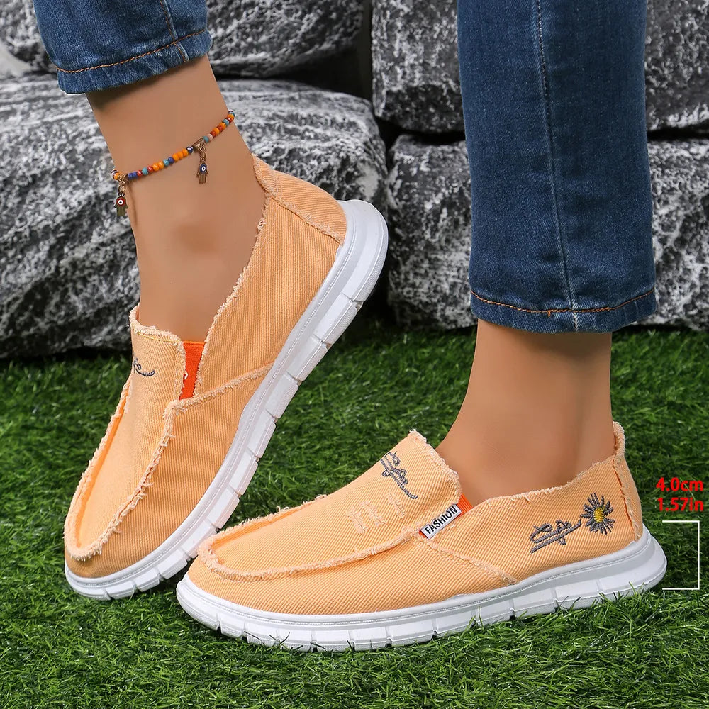 Raw-edge embroidered canvas slip-ons in sherbet with floral detail and white soles.