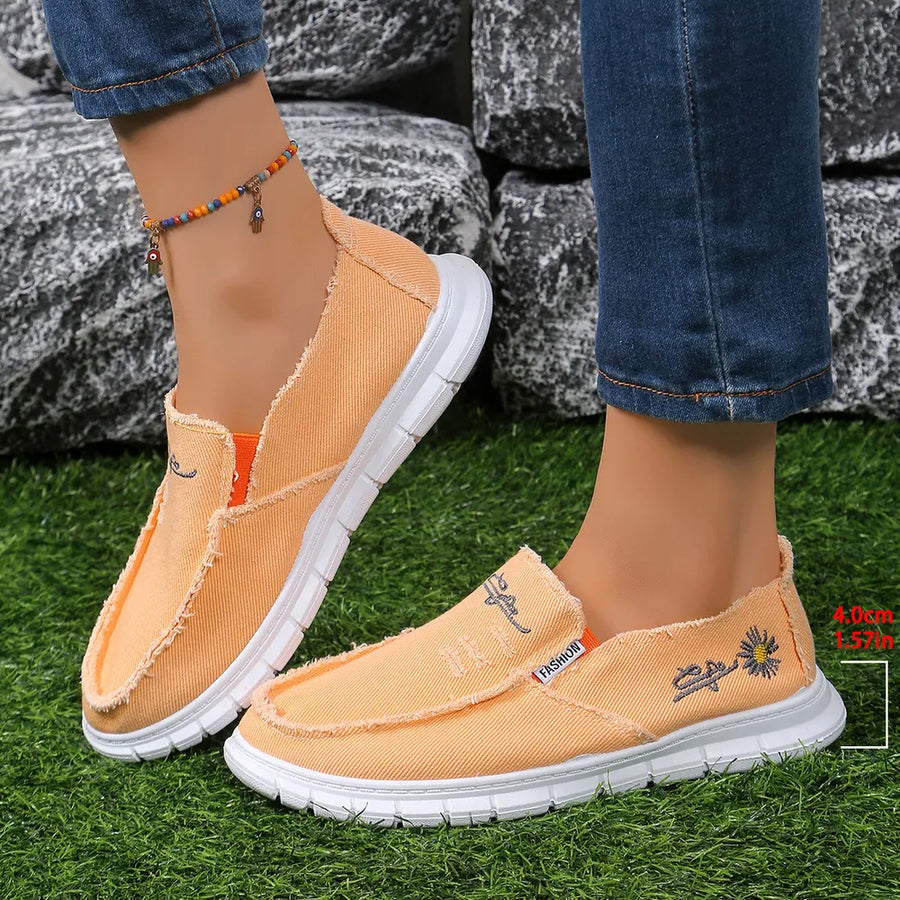 Raw-edge embroidered canvas slip-ons in sherbet with floral detail and white soles.