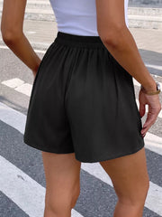 Black high-waisted pleated chino shorts with elastic waistband and decorative button detail.