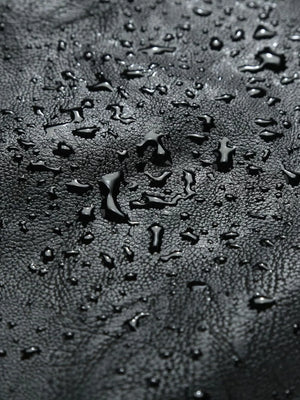 Black moto jacket material with water droplets, showing texture.