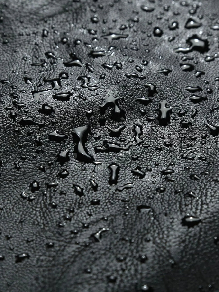 Black moto jacket material with water droplets, showing texture.