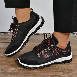 Black low-top sneakers with red patterned laces and white soles.