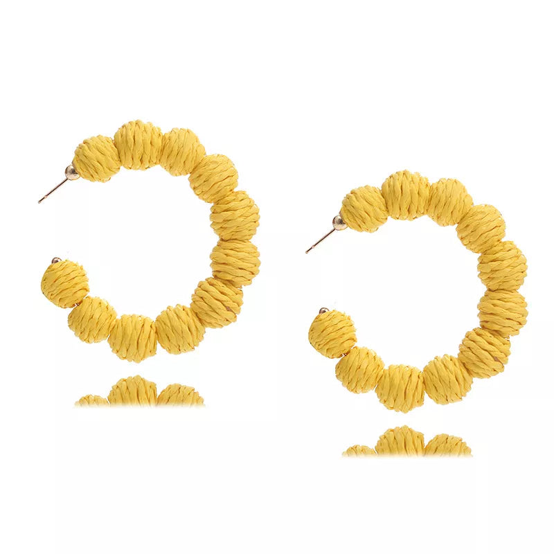 Yellow raffia grass C-hoop earrings with textured ball details.