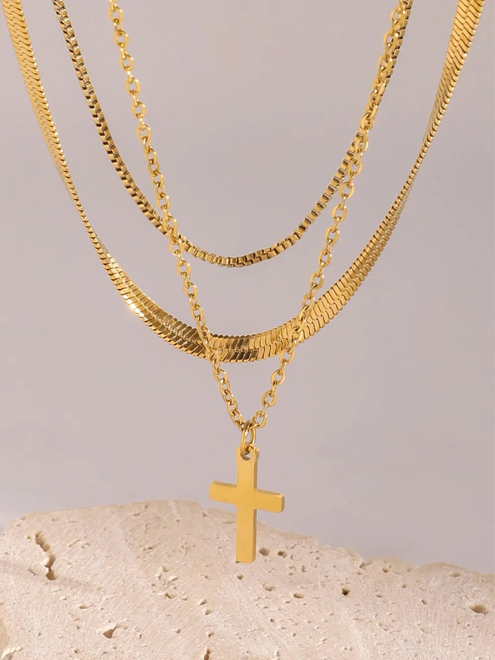 Gold layered necklace with snake and box chains, featuring a cross pendant.