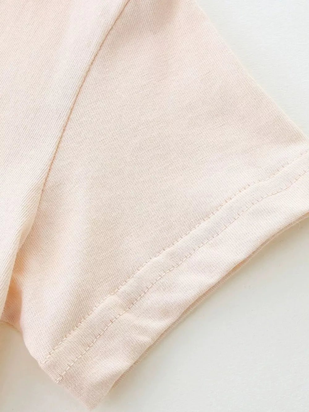 Baby dress sleeve detail in pale pink cotton with double-stitched hem.