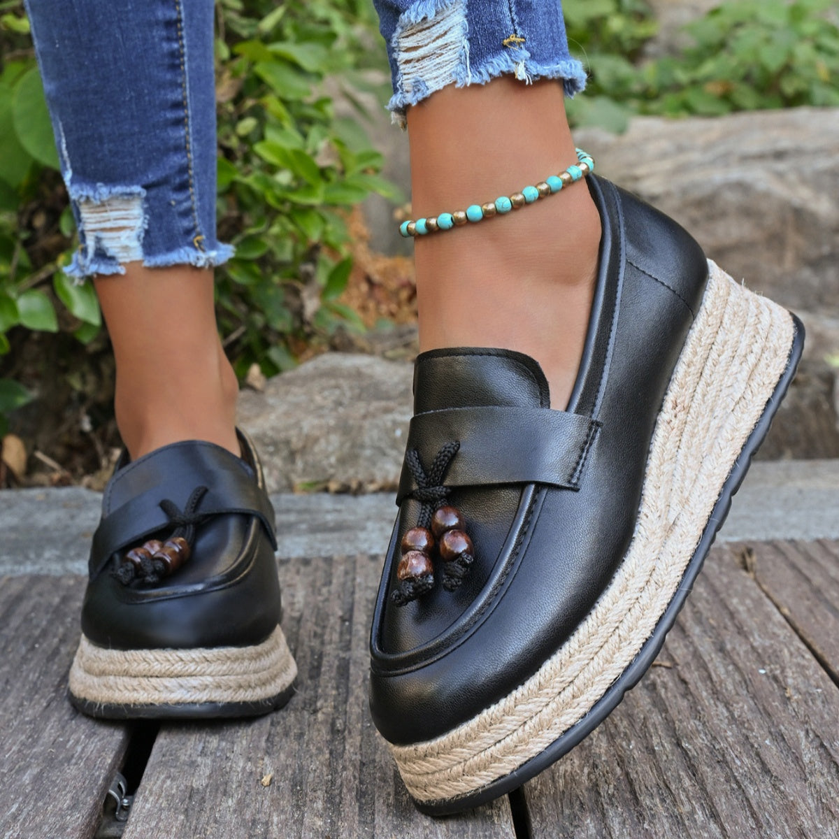 Black espadrille wedge slip-on loafers with braided jute soles and tassel detail.