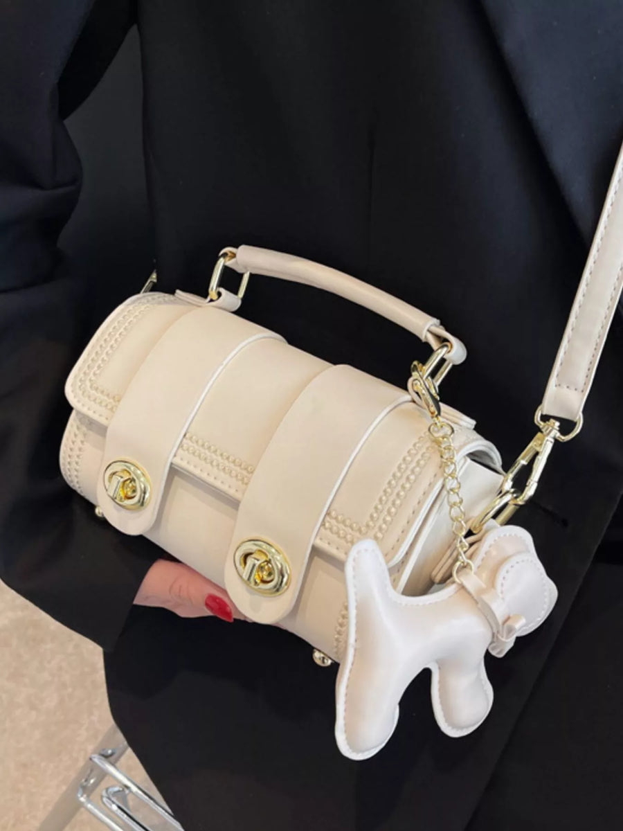 Mini beige PU leather crossbody bag with gold hardware and dog charm accessory.