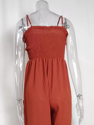 Orange-red smocked wide leg romper with spaghetti straps and pockets.