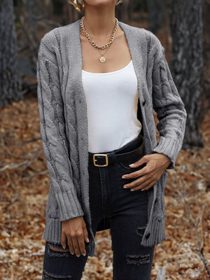Grey cable knit cardigan with button front and pockets, worn over a white tank top.