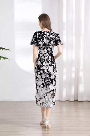 Black midi dress with white floral embroidery, short sleeves, and sheer hem.