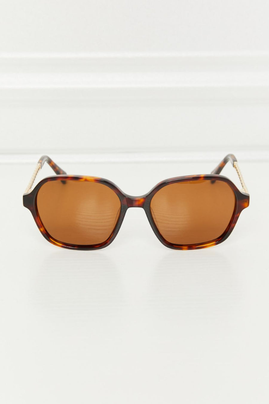 Brown tortoiseshell hexagonal frame sunglasses with gold accents on temples.