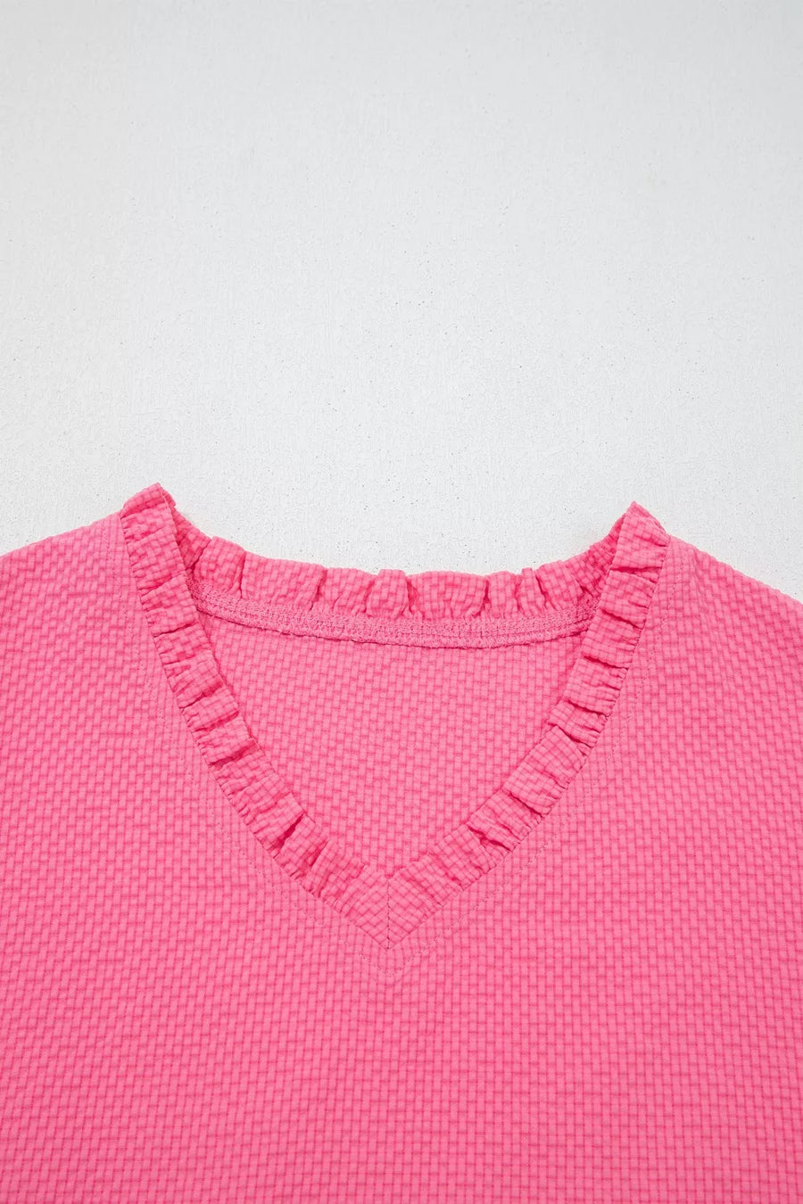 Women's pink textured V-neck blouse with ruffled neckline detail