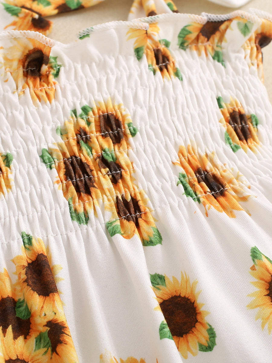 Baby jumpsuit with white cotton and yellow sunflower print, featuring smocked bodice.