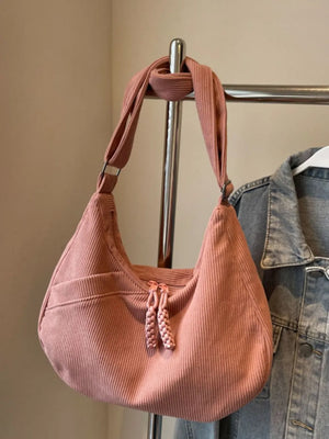 Pink corduroy crescent shoulder bag with braided zipper tassels and front pocket.