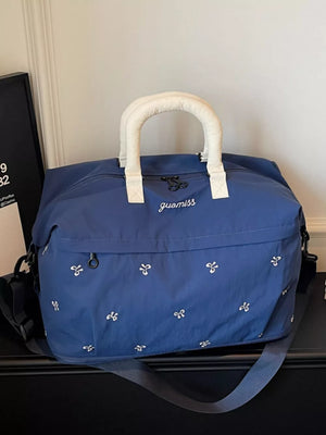 Blue duffel bag with white embroidered bows and padded cream handles