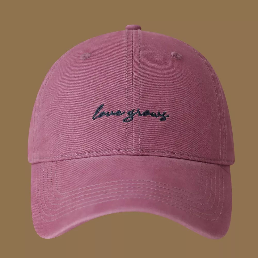 Raspberry purple cotton baseball cap with embroidered "love grows" text.