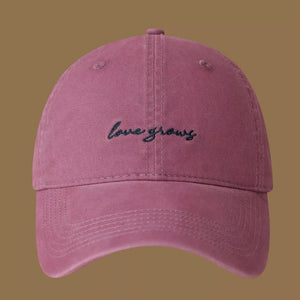 Raspberry purple cotton baseball cap with embroidered "love grows" text.