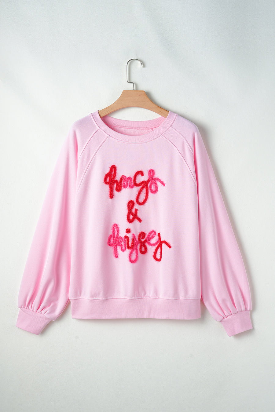 Blush pink sweatshirt with embroidered "hugs & kisses" graphic and balloon sleeves.