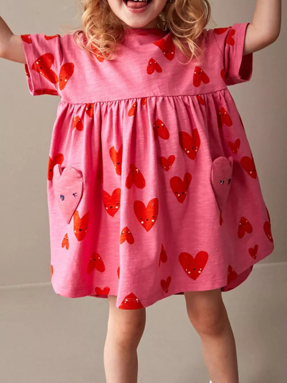 Pink cotton baby dress with red heart print and functional pockets.